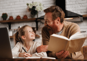 Vader en dochter die samen een boek lezen en lachend naar kijkend